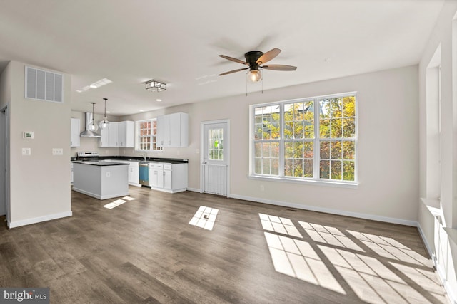 kitchen featuring wall chimney range hood, hardwood / wood-style flooring, a center island, decorative light fixtures, and white cabinetry