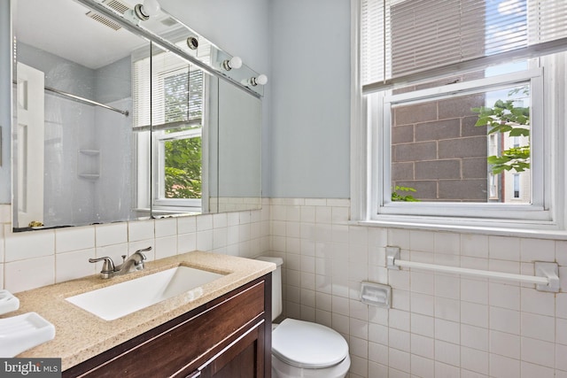 bathroom with tile walls, plenty of natural light, vanity, and toilet