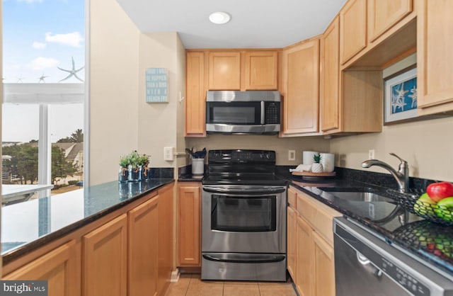 kitchen featuring dark stone countertops, sink, light tile patterned floors, and appliances with stainless steel finishes