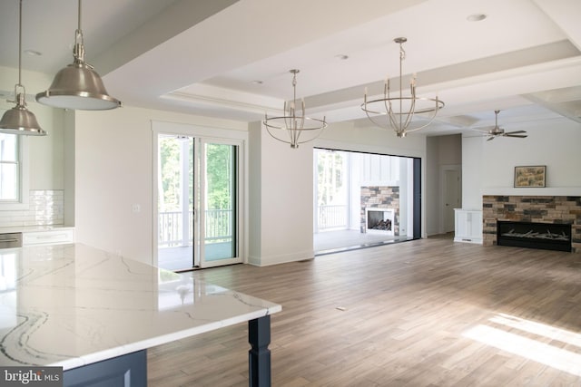 interior space with ceiling fan with notable chandelier, a fireplace, wood-type flooring, and a raised ceiling