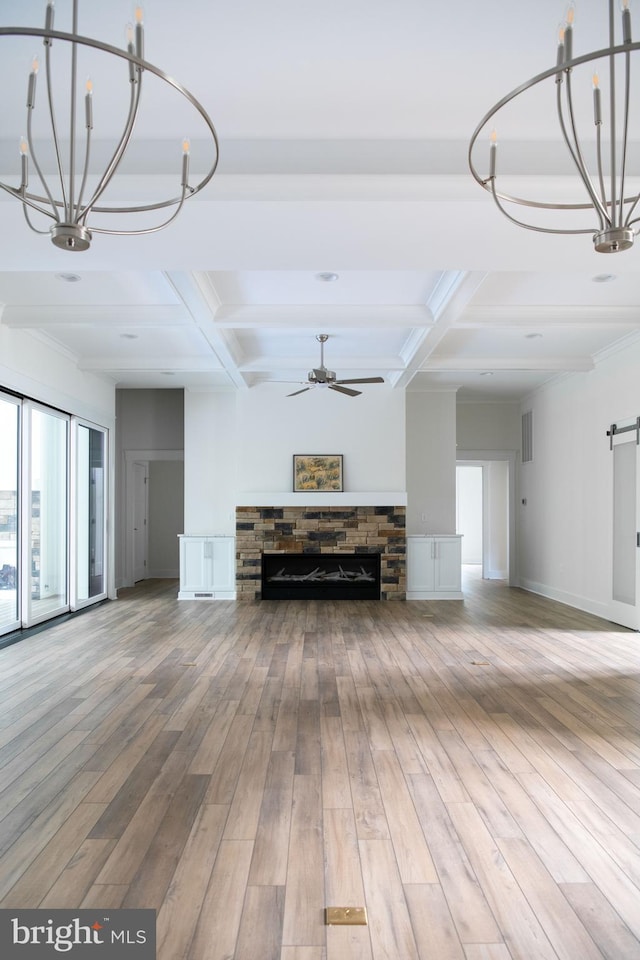 unfurnished living room featuring beamed ceiling, ceiling fan with notable chandelier, coffered ceiling, hardwood / wood-style floors, and a stone fireplace