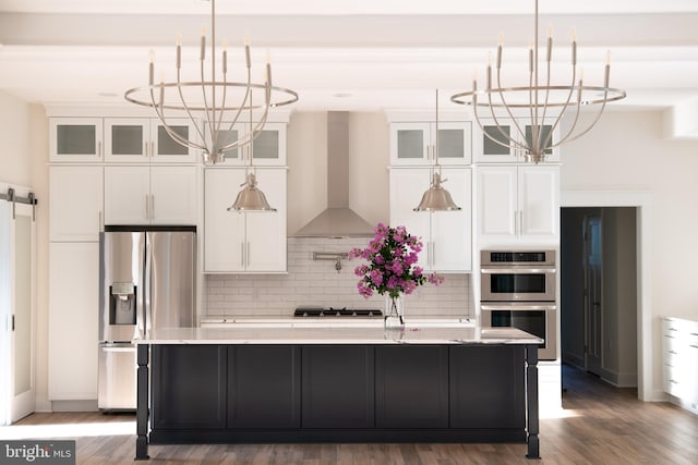 kitchen with wall chimney exhaust hood, appliances with stainless steel finishes, hardwood / wood-style flooring, and a kitchen island with sink