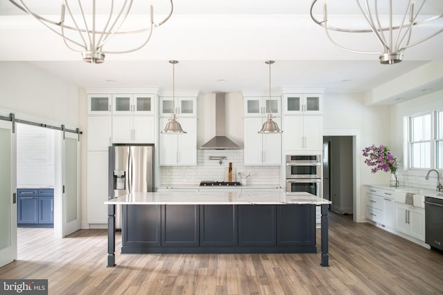 kitchen with a barn door, wall chimney exhaust hood, a large island, and appliances with stainless steel finishes