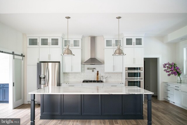 kitchen featuring hanging light fixtures, backsplash, wall chimney range hood, white cabinetry, and appliances with stainless steel finishes