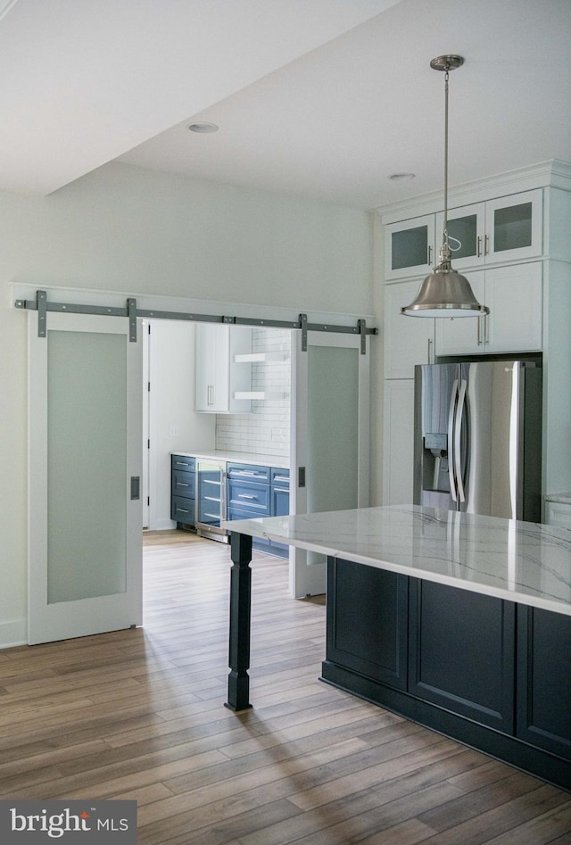 kitchen with light hardwood / wood-style flooring, white cabinets, stainless steel fridge with ice dispenser, and a barn door