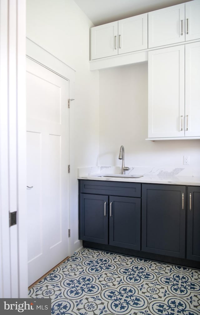 bar featuring light stone counters, sink, and white cabinetry