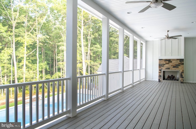 unfurnished sunroom with ceiling fan and a stone fireplace