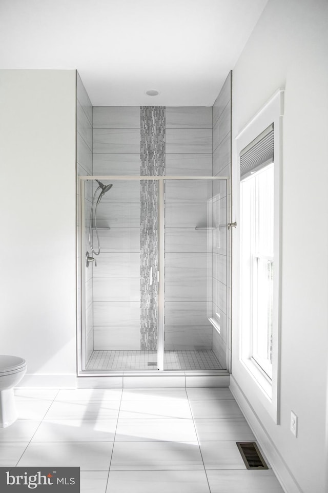 bathroom featuring toilet, a shower with door, and tile patterned floors