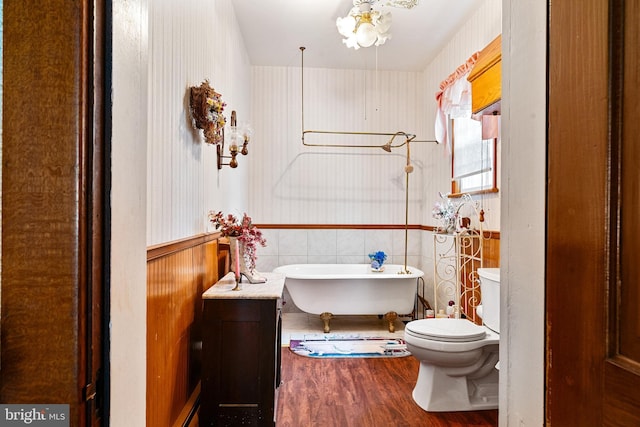 full bathroom with a freestanding tub, toilet, wood finished floors, wainscoting, and wallpapered walls