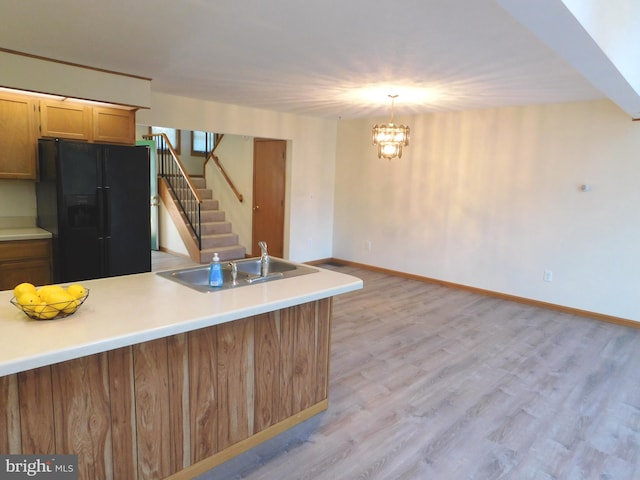 kitchen with black fridge with ice dispenser, pendant lighting, light wood-type flooring, sink, and a chandelier