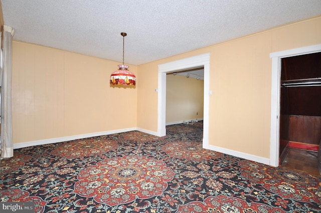 unfurnished dining area with a textured ceiling, dark carpet, and baseboards