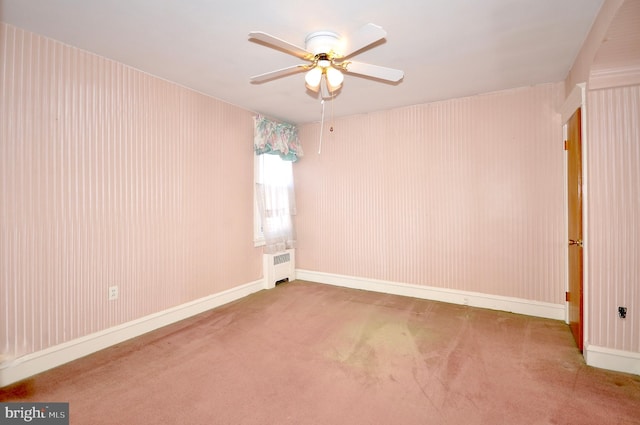 carpeted empty room featuring ceiling fan, radiator heating unit, and baseboards