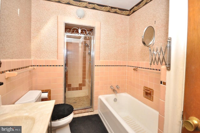 full bath featuring a garden tub, tile walls, toilet, wainscoting, and wallpapered walls