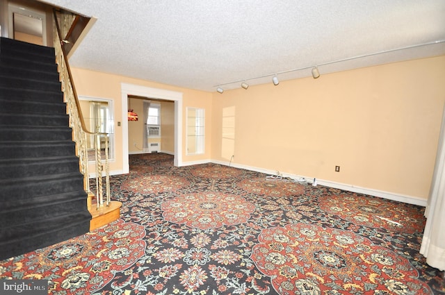 empty room with a textured ceiling, baseboards, stairway, carpet, and track lighting