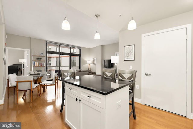 kitchen featuring a kitchen breakfast bar, light hardwood / wood-style flooring, a center island, pendant lighting, and white cabinetry