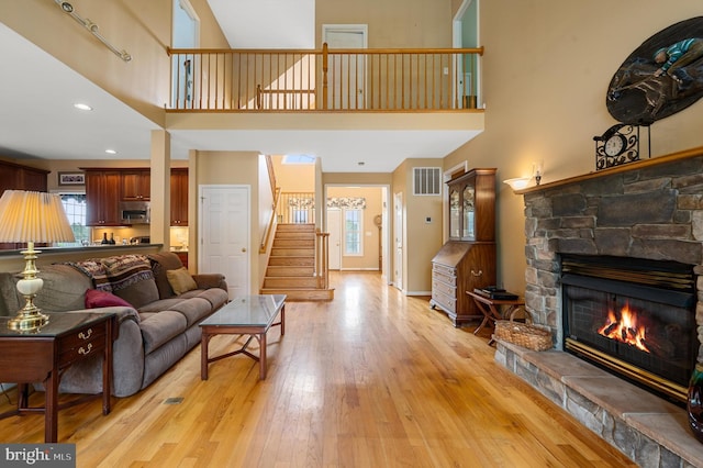 living room with a high ceiling, a stone fireplace, and light hardwood / wood-style flooring