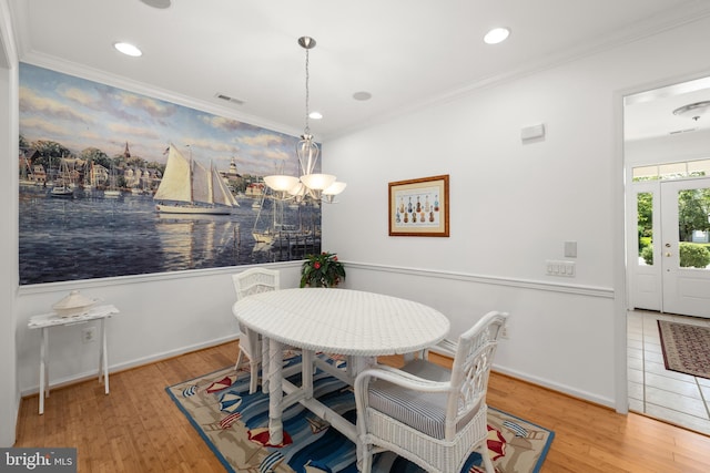 dining space with light hardwood / wood-style flooring, ornamental molding, and an inviting chandelier