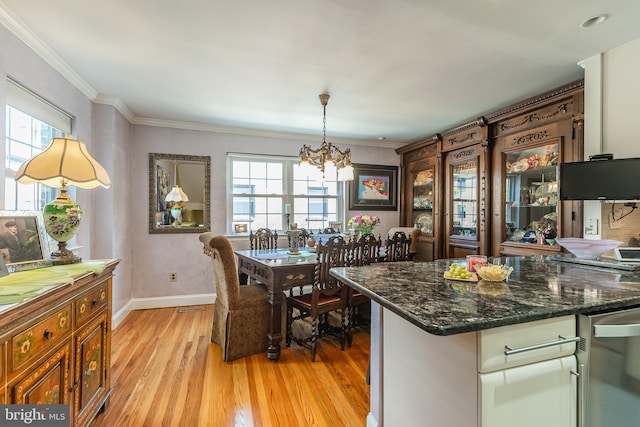 kitchen with crown molding, dark stone counters, hanging light fixtures, an inviting chandelier, and light hardwood / wood-style floors