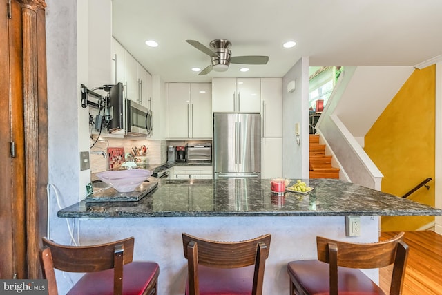 kitchen with stainless steel appliances, a breakfast bar, white cabinets, light hardwood / wood-style floors, and kitchen peninsula