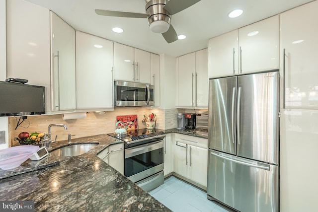 kitchen with white cabinetry, appliances with stainless steel finishes, backsplash, sink, and dark stone countertops