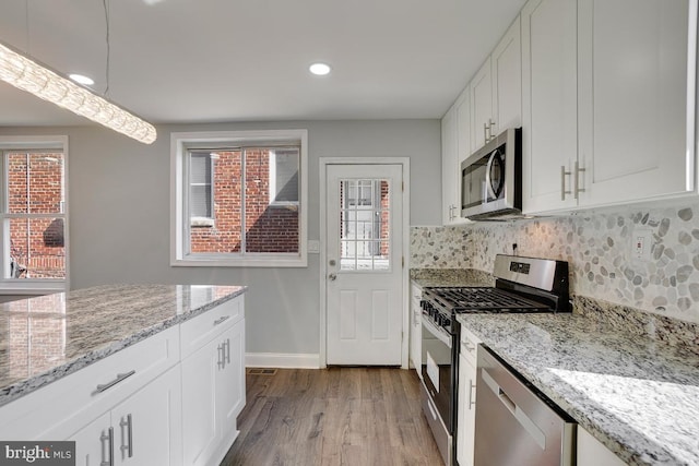 kitchen with light stone countertops, light hardwood / wood-style flooring, appliances with stainless steel finishes, tasteful backsplash, and white cabinetry