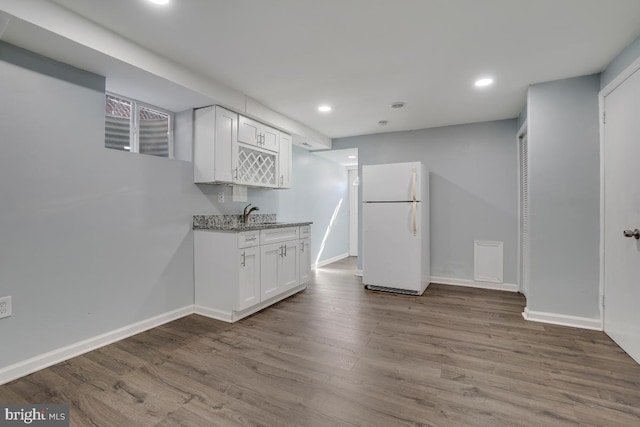 kitchen with white cabinets, white fridge, light stone counters, and light hardwood / wood-style floors