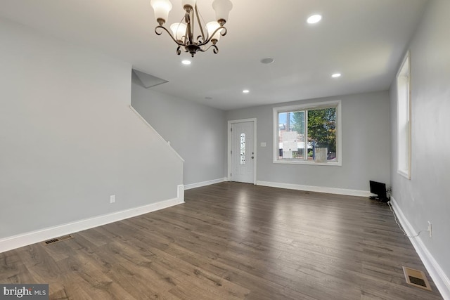 empty room with dark wood-type flooring and an inviting chandelier