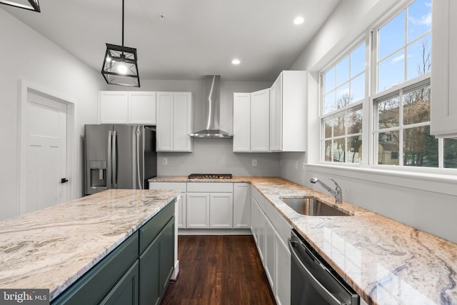 kitchen featuring wall chimney exhaust hood, sink, decorative light fixtures, white cabinetry, and appliances with stainless steel finishes