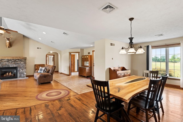 dining space featuring light wood-type flooring, a stone fireplace, vaulted ceiling, and a chandelier