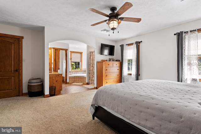 bedroom featuring ensuite bath, multiple windows, light colored carpet, and ceiling fan