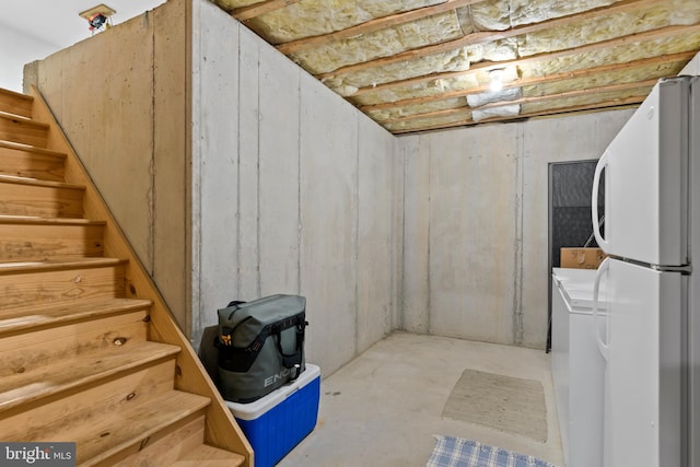 basement featuring stacked washer / drying machine and white fridge