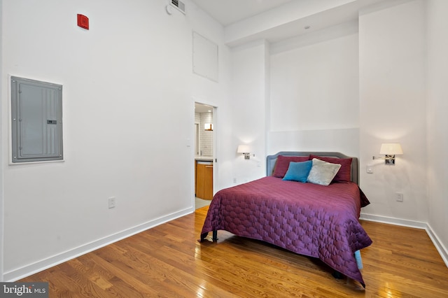 bedroom featuring wood-type flooring, a towering ceiling, and electric panel