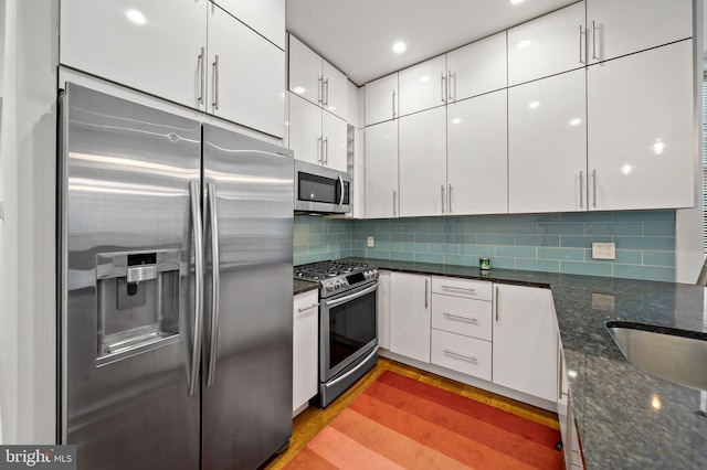 kitchen featuring dark stone counters, stainless steel appliances, white cabinetry, and light hardwood / wood-style flooring