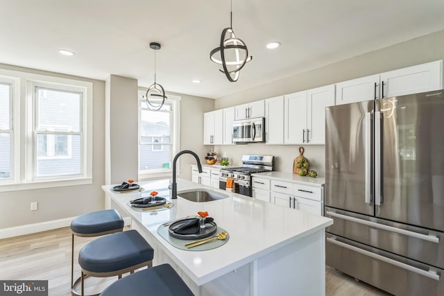 kitchen featuring sink, white cabinetry, light hardwood / wood-style flooring, appliances with stainless steel finishes, and decorative light fixtures