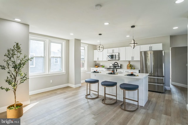 kitchen featuring white cabinets, a center island with sink, appliances with stainless steel finishes, and light wood-type flooring