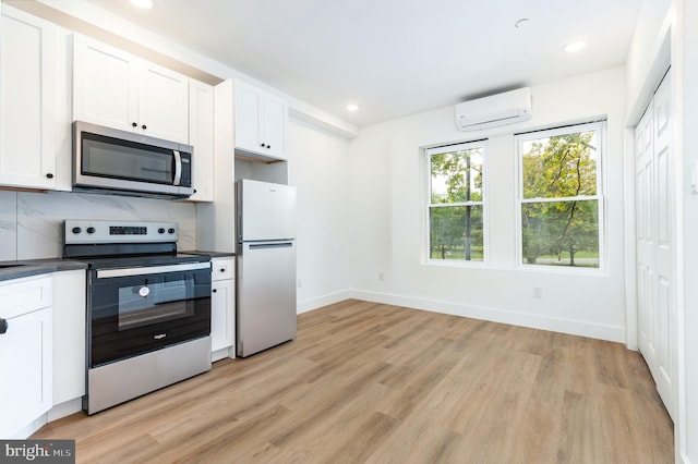 kitchen featuring appliances with stainless steel finishes, white cabinetry, light hardwood / wood-style flooring, and a wall unit AC