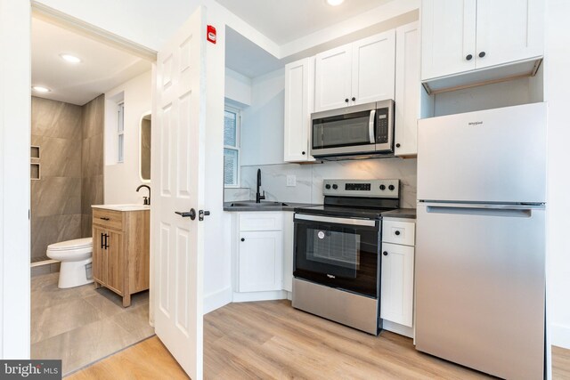 kitchen featuring appliances with stainless steel finishes, light wood-type flooring, sink, and white cabinets