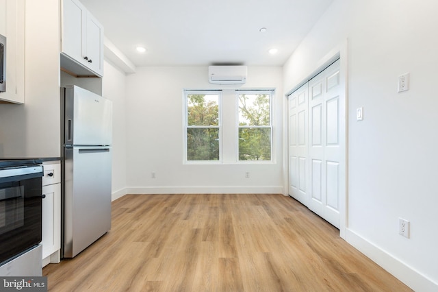 kitchen featuring white cabinets, appliances with stainless steel finishes, light hardwood / wood-style flooring, and an AC wall unit