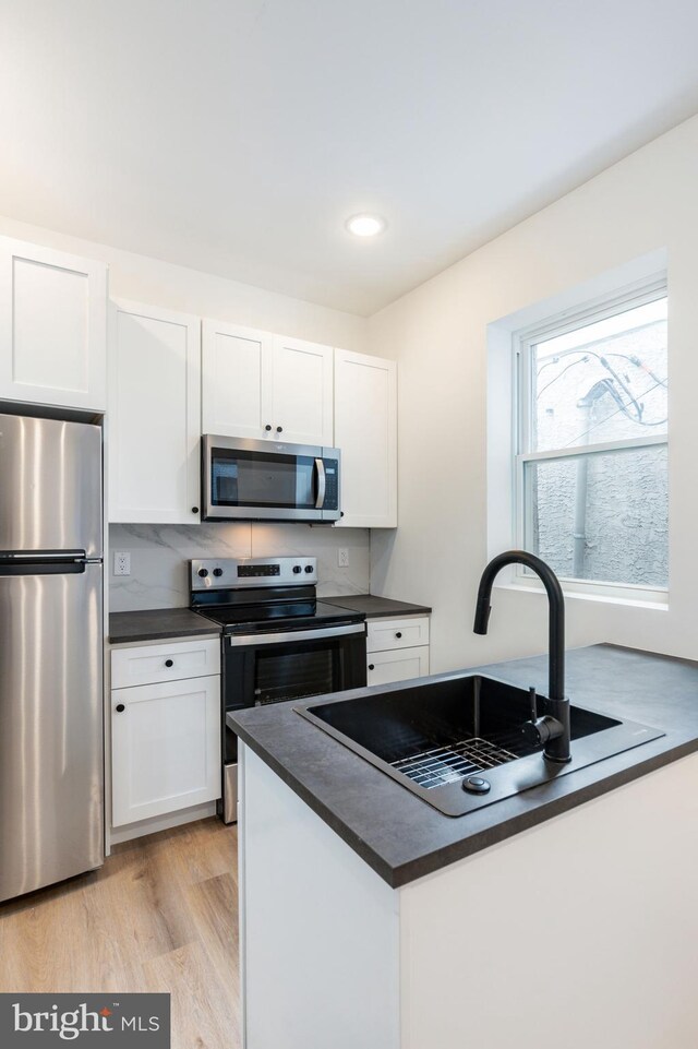 kitchen featuring stainless steel appliances, white cabinets, light wood-type flooring, and sink