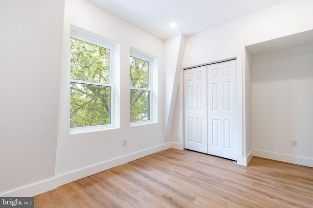 unfurnished bedroom with a closet, light wood-type flooring, and multiple windows