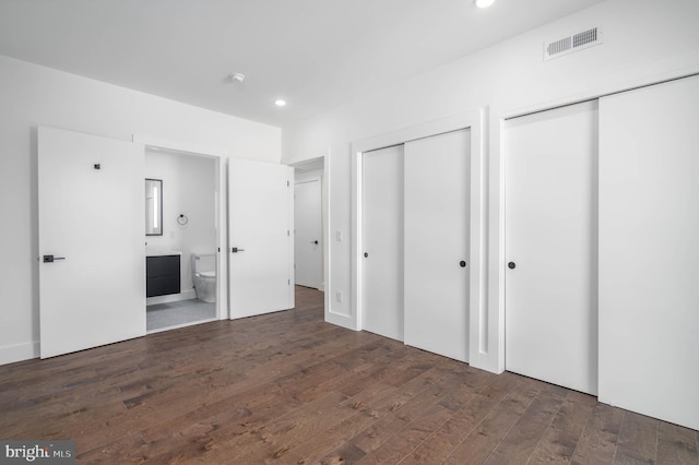 unfurnished bedroom with two closets, dark hardwood / wood-style flooring, and ensuite bathroom