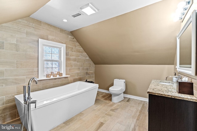 bathroom with a bathing tub, hardwood / wood-style flooring, vaulted ceiling, vanity, and toilet