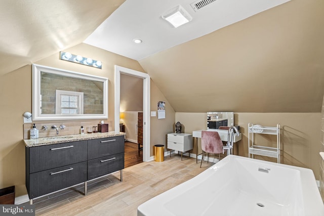 bathroom featuring hardwood / wood-style floors, vaulted ceiling, a tub, and vanity