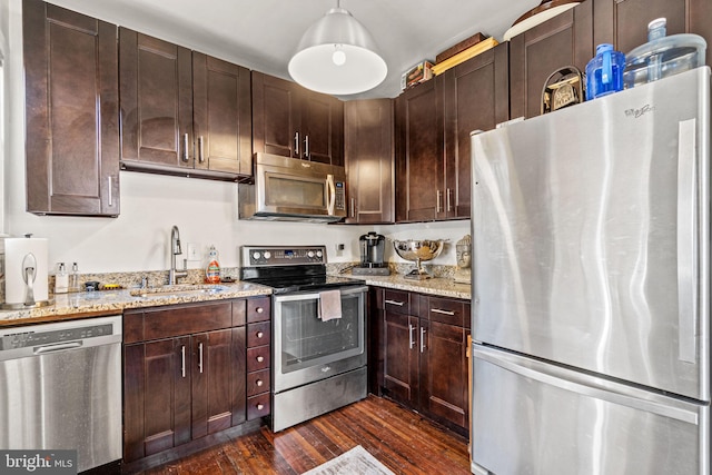 kitchen with light stone counters, sink, decorative light fixtures, dark wood-type flooring, and appliances with stainless steel finishes