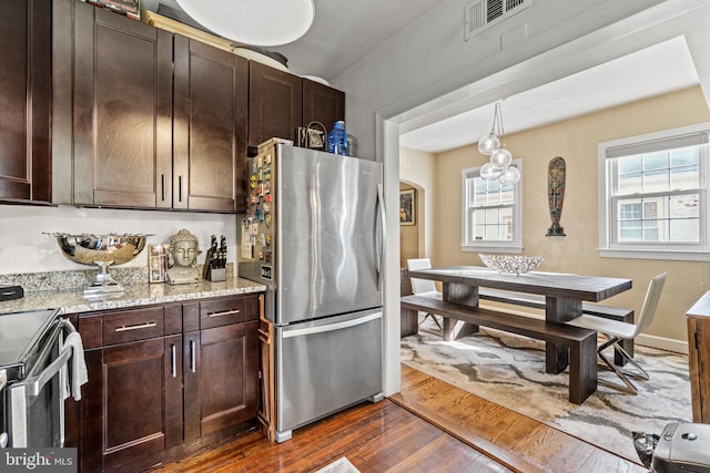 kitchen with light stone counters, hanging light fixtures, dark brown cabinets, stainless steel appliances, and dark hardwood / wood-style flooring