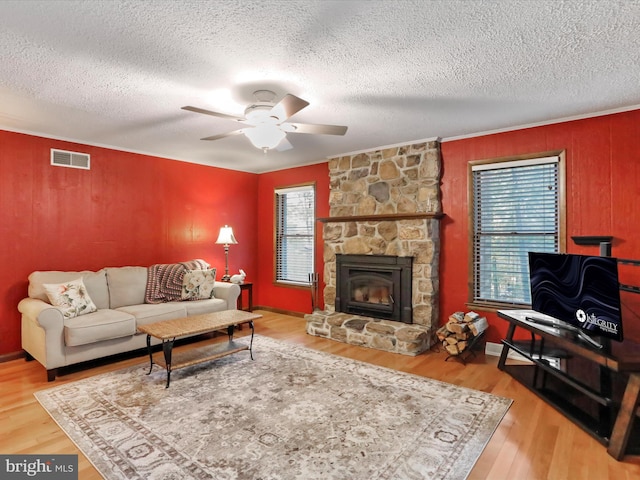 living room with ceiling fan, wood-type flooring, a stone fireplace, and a textured ceiling