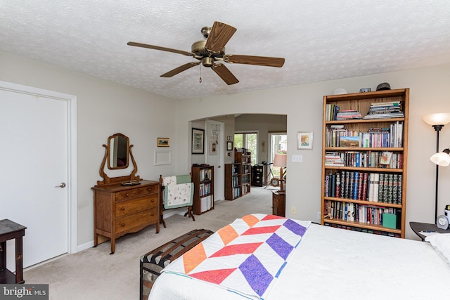 bedroom featuring ceiling fan, light colored carpet, and a textured ceiling