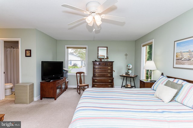 bedroom with light carpet, connected bathroom, multiple windows, and ceiling fan