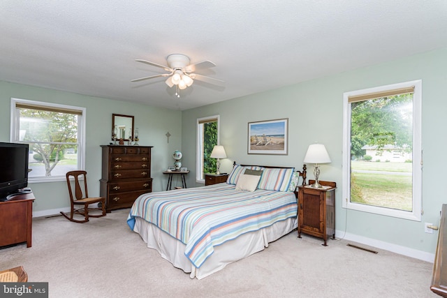 bedroom with ceiling fan, light colored carpet, and a textured ceiling