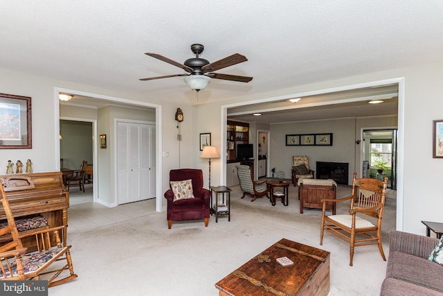 living room featuring ceiling fan, light colored carpet, and a textured ceiling